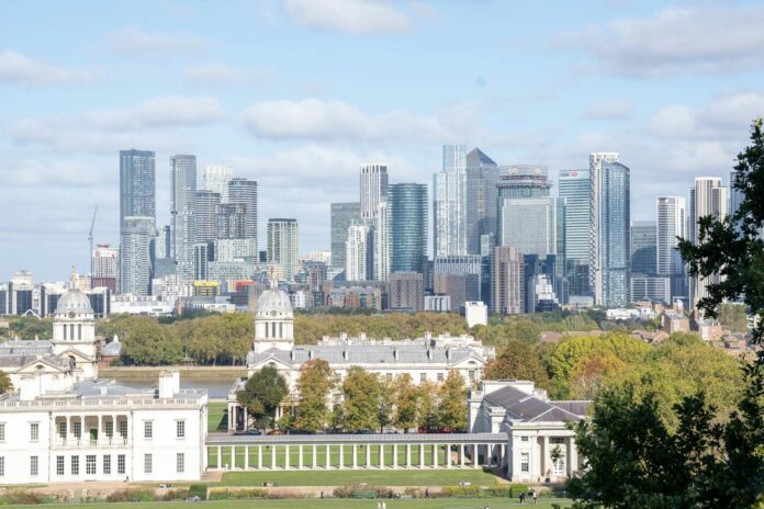 A scenic view of the Canary Wharf skyline from Greenwich Park, featuring iconic skyscrapers and lush greenery.