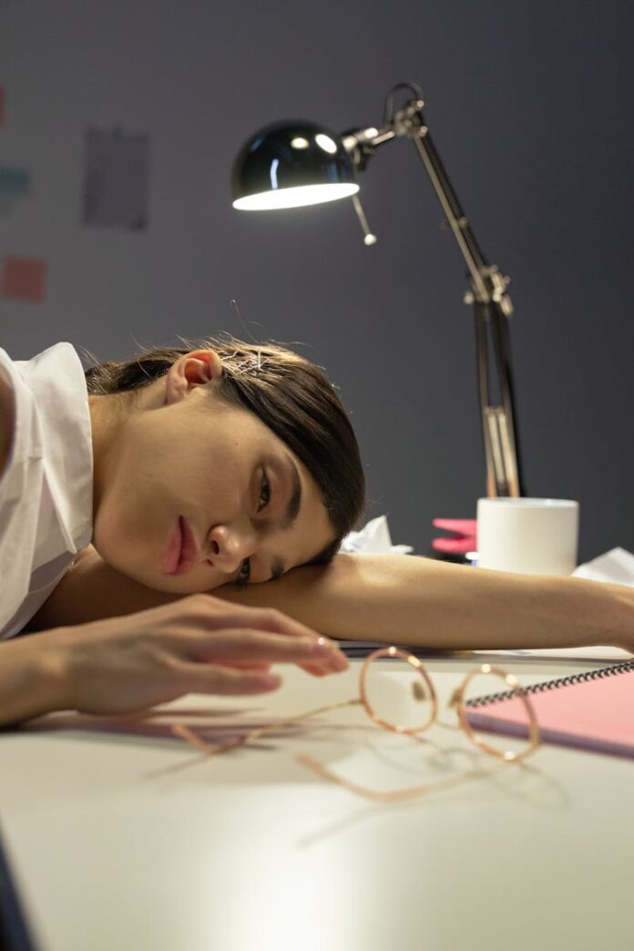 Tired woman resting head on desk with a lamp, representing stress and exhaustion.
